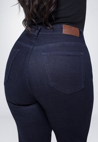 Donkerblauwe spijkerbroek met een hoge taille, voorzien van een leren logo-label en twee achterzakken. Glad textuur en een slim fit ontwerp.