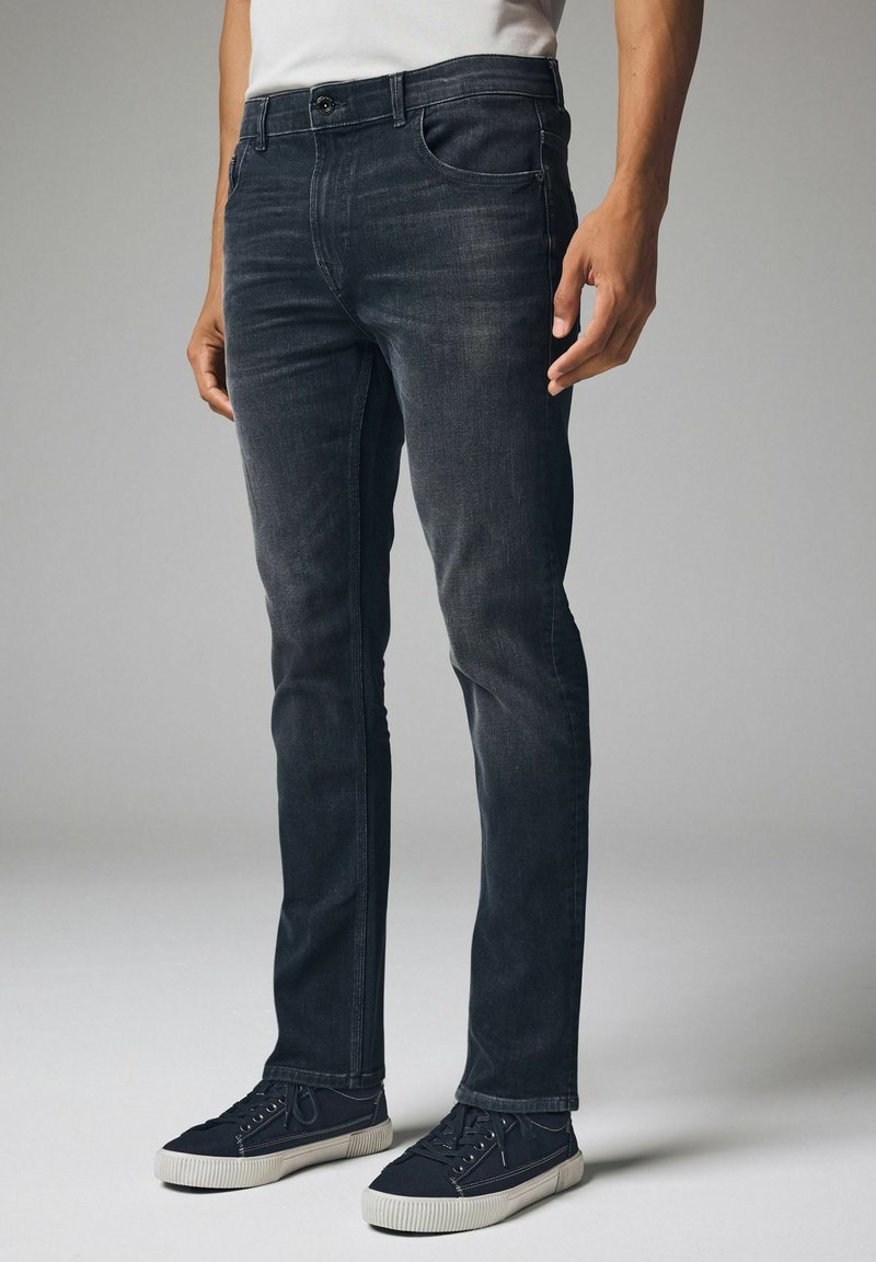 Sötét indigo slim-fit farmernadrág, elhalványult felülettel, öt zsebbel és cipzáras felszereléssel. Fekete vászon tornacipővel párosítva.