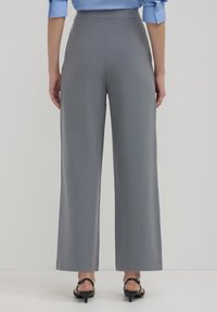 Weite graue Hosen mit glatter Textur und hohem Bund. Klare Linien und minimale Details, kombiniert mit schwarzen Riemchen-Heels.