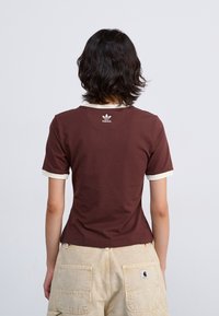 Brown short-sleeve t-shirt with cream accents at the collar and sleeves, featuring a small white Adidas logo at the back.