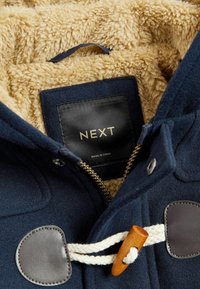 Donkerblauwe fleece jas met een beige nepbont voering. Bevat bruine leren accenten en een houten sluiting met touw. Etiket zegt "NEXT."