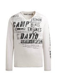 Langarmhemd in creme mit schwarzem Drucktext und Grafiken. V-Ausschnitt-Design mit strukturierter Oberfläche und kontrastierender Naht.