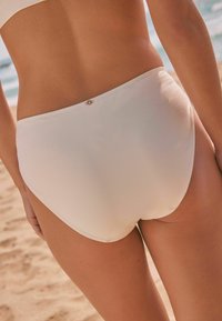 Hellbeige, hoch geschnittene Bikinihose mit glatter Textur, minimaler Naht und einem kleinen Logodetail auf der Rückseite.