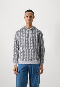Felpa grigia con un motivo geometrico nero, dotata di tasca frontale, cappuccio con cordino e polsini a costine. Abbinata a pantaloni cargo blu.