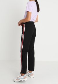 Svarta byxor med röda och vita sidostripes, tillverkade av slät tyg. Matchade med en lila skjorta och vita sneakers. Rakt ben-design.