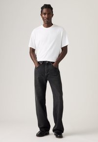 Λευκό κοντομάνικο μπλουζάκι συνδυασμένο με φαρδιά μαύρα τζιν και μαύρα παπούτσια. Το σύνολο χαρακτηρίζεται από casual σχεδιασμό με χαλαρή σιλουέτα.