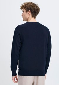 Suéter de punto azul marino con mangas largas, puños y dobladillo acanalados, que presenta un cuello redondo y una textura limpia y suave.