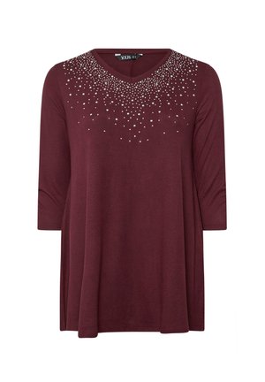 Burgundy tunika dengan lengan tiga suku, garis leher V, dan dihiasi dengan paku perak dalam pola gradasi di bagian depan atas.