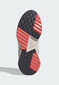 La suela de goma del zapato presenta una superficie negra texturizada con acentos de rayas rojas y una marca, diseñada para ofrecer tracción y durabilidad.