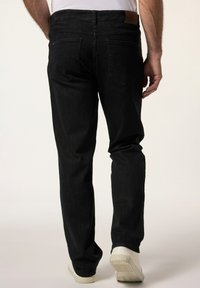 Schwarze Jeans aus Denim mit geradem Schnitt, ausgestattet mit zwei Gesäßtaschen und einem braunen Lederpatch am Bund. Getragen mit weißen Schuhen.