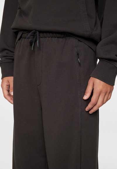 Pantalons de jogging gris foncé en tissu doux, avec une taille élastique à cordon de serrage et une poche zippée sur le côté.