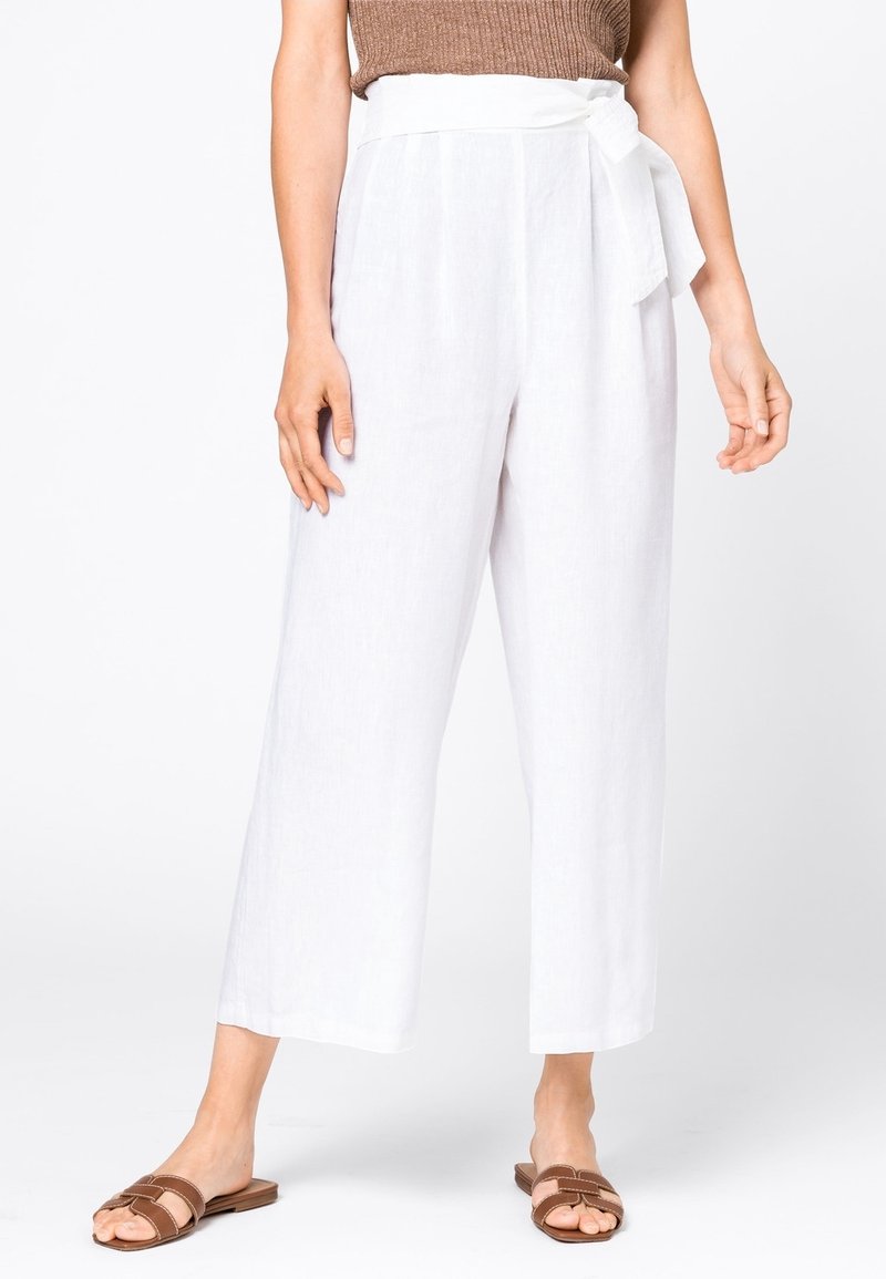 Femme portant un pantalon blanc taille haute à jambes larges avec une ceinture à nouer sur le côté, associé à un top marron sans manches et des sandales marron plates.