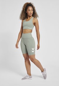 Lichtgroene sportbeha en hoge shorts met witte chevronpatronen. Gecombineerd met grijze sportschoenen en een gladde, elastische textuur.