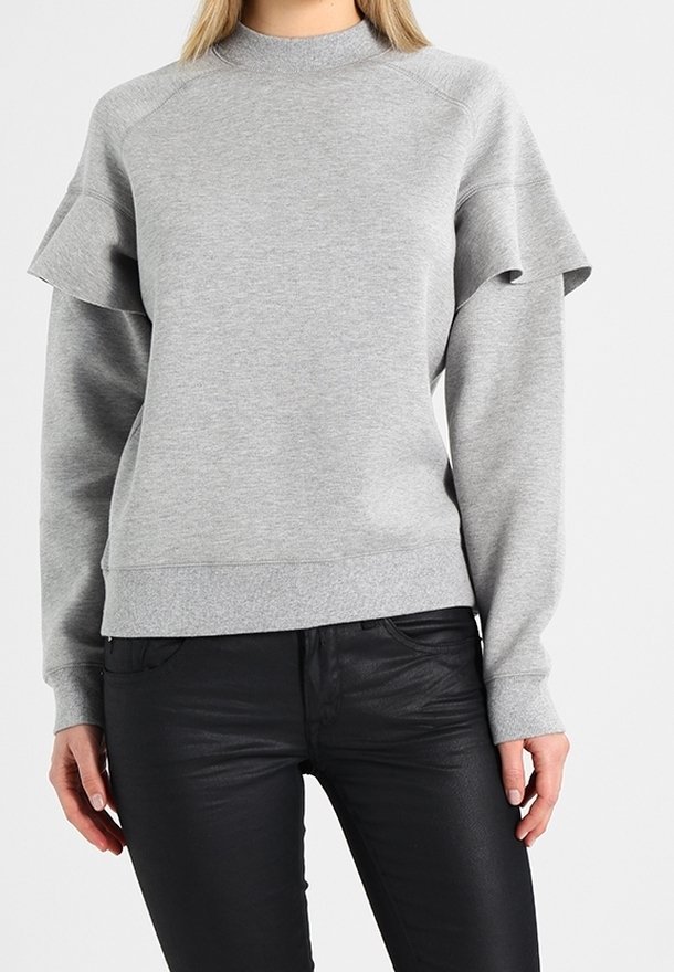 Szary sweatshirt wykonany z miękkiego materiału, z wysokim kołnierzem i rękawami raglanowymi. Zauważalny falbany na rękawach, zestawiony z czarnymi spodniami.