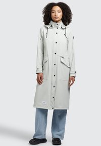 Light gray waterproof coat with a high collar, drawstring hood, and large front pockets. Features snap buttons and a branded patch.