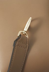 Bruine leren schouderriem met gouden hardware details, voorzien van een clip en een in reliëf aangebracht "Valentino" logo aan de zijkant. Glad van structuur.