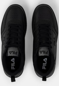 Baskets de sport noires en matériau synthétique avec une texture lisse, un design à lacets et une zone de orteil perforée. Logo visible sur la languette.