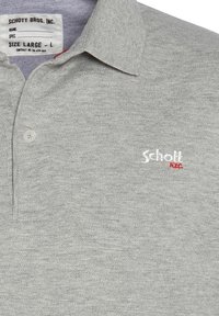 Polo gris en tissu texturé, avec un col à deux boutons et un petit logo brodé "Schott NYC" en blanc et rouge.