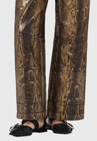 Brązowe spodnie w wzór wiskozy z teksturowanego materiału, w połączeniu z czarnymi butami typu slip-on z ozdobnym złotym zapięciem.