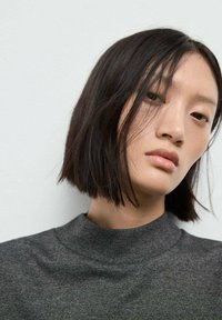 Top în nuanță de gri închis, cu guler înalt, confecționat dintr-un material moale, având o textură fină și un design casual, purtat de un model cu păr drept, de culoare neagră.