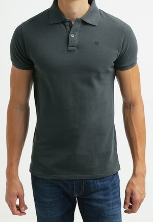 Ciemnoszara koszulka polo z bawełny o fakturowanym wykończeniu, z patką na trzy guziki i małym logo na piersi. W zestawie z niebieskimi jeansami.