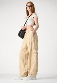 Light beige cargo pants with a relaxed fit, featuring side pockets and elastic waistband. Worn with a white crop top and white sneakers.