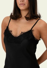 Camisolă neagră cu margine din dantelă având un design valurit de-a lungul liniei gâtului, cu bretele subțiri ajustabile și o textură fină a țesăturii.