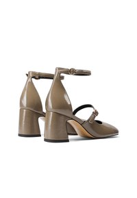 Tacchi in pelle lucida beige con punta chiusa, cinturino alla caviglia e tacco a blocco. Presentano un design con ritagli e un dettaglio in fibbia dorata.