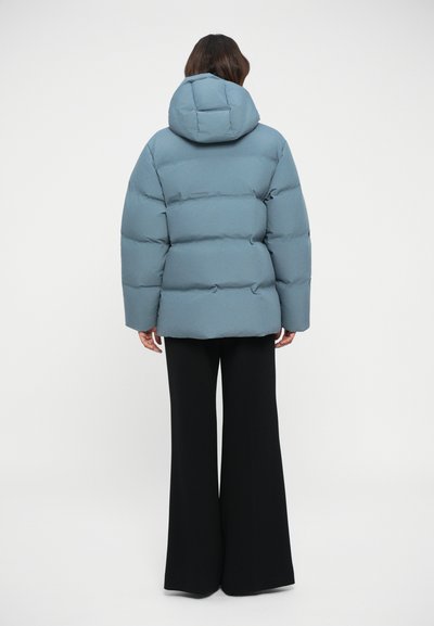 Svetlo modra puhovka z kapuco, z n stitched sekcijami, nosi se preko črnih širokih hlač. Gladka tekstura, sproščen kroj.