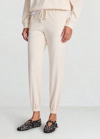 Pantalon de jogging crème clair avec taille élastique, chevilles resserrées et texture lisse, associé à des chaussures noires avec œillets métalliques.