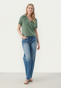 Grøn kortærmet polo skjorte med V-hals, parret med lyseblå lige ben jeans. Sandaler fuldender det afslappede outfit.