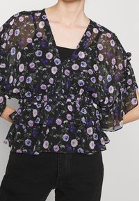 Blusa nera floreale con maniche corte a volant, decorata con fiori viola e bianchi, scollo a V e una fascia elastica in vita con design a peplum.