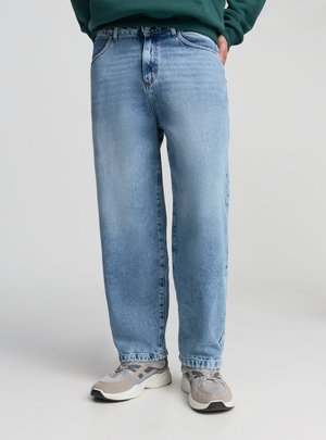 Jeans denim blu chiaro a taglio ampio con un design classico a cinque tasche. Il tessuto presenta una texture sbiadita e lievi effetto usurato. Abbinati a sneakers grigie.