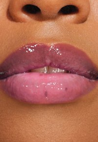 Labios brillantes y bicolores presentan un degradado de ciruela profunda a rosa suave, mostrando una textura suave y un brillo sutil sobre la piel.