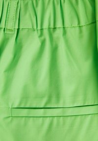 Tessuto verde brillante con una trama liscia, dotato di una cintura elastica e di una tasca orizzontale cucita nel design.