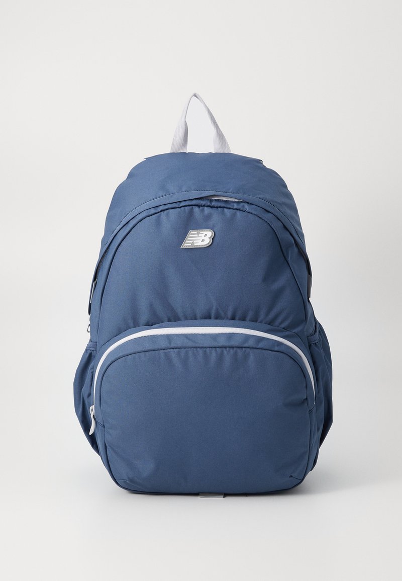 Sac à dos bleu marine avec une structure rembourrée, poche frontale zippée et accents gris. Présente un logo et une poignée de transport supérieure. Texture de tissu lisse.