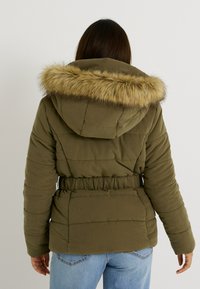 Chaqueta acolchada verde oliva con capucha de piel sintética, cinturilla elástica y diseño acolchado; presenta un ajuste holgado y mangas largas.