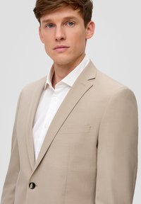 Beige Sakko aus strukturiertem Stoff mit einem Ein-Knopf-Verschluss, Reverskragen und einer Brusttasche, kombiniert mit einem weißen Hemd.