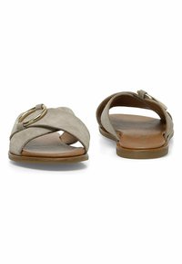 Sandalias de ante con un diseño entrecruzado, color beige, punta descubierta y un acento decorativo de anillo dorado. Suela plana con un acabado suave.