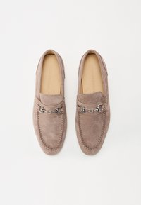 Taurējo suede loaferi pelēkā krāsā ar noapaļotu purngalu, dekoratīvu sudraba ķēdes aparatūru pāri priekšdaļai un kontrastējošiem šuvju izstrādājumiem.