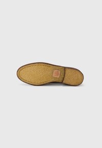 Braune Schuhsohle aus strukturiertem Gummi mit einem hellen Korkakzent in der Nähe der Ferse. Glatte Kanten und geschwungene Form im Bereich der Zehen.