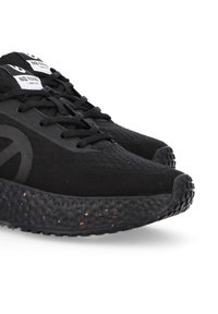 Schwarze Sportschuhe mit einem strukturierten Strickobermaterial und Gummisohle, ausgestattet mit einem markanten gesprenkelten Muster auf der Sohle und schwarzen Schnürsenkeln.