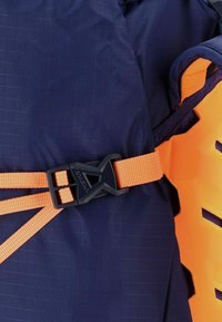 Tessuto blu navy con una trama a griglia presenta una tracolla regolabile arancione e una fibbia in plastica nera. Gli accenti sono evidenziati in colori contrastanti.
