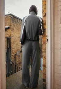 Gray tracksuit with a zip-up jacket featuring white and black accents, paired with loose-fitting, elastic-waist pants. Textured background.