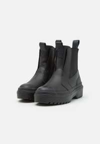Botas Chelsea negras de cuero con paneles laterales elásticos, punta redondeada y suela de goma gruesa con un patrón texturizado.