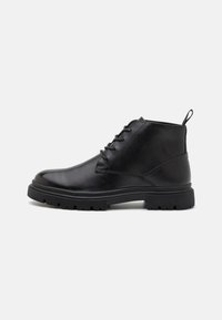 Botas de cuero negras hasta el tobillo con cordones en la parte delantera, suela texturizada y asa de tiro. Punta redondeada y suela de goma robusta que mejora la tracción.