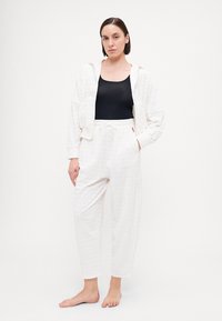 Witte gebreide hoodie en bijpassende joggers, met een koordtaille, zachte stof en een losse pasvorm. Zwarte tanktop eronder.