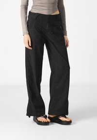 Black wide-leg cargo pants made of cotton blend fabric, featuring two side pockets, button closure, and reinforced stitching details.