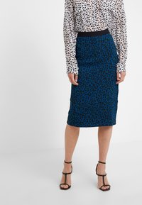 Blue leopard print pencil skirt with a black waistband. Paired with a white blouse featuring a black abstract pattern and long sleeves.
