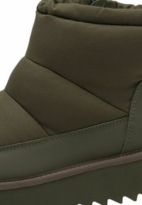 Puffiger olivgrüner Stiefel mit strukturiertem Obermaterial, diagonal genäht und mit einer dicken Gummisohle mit Zickzackmuster für besseren Halt.